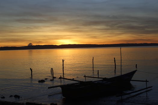 A serene sunrise scene featuring a boat silhouette on a calm sea, evoking peace and tranquility.