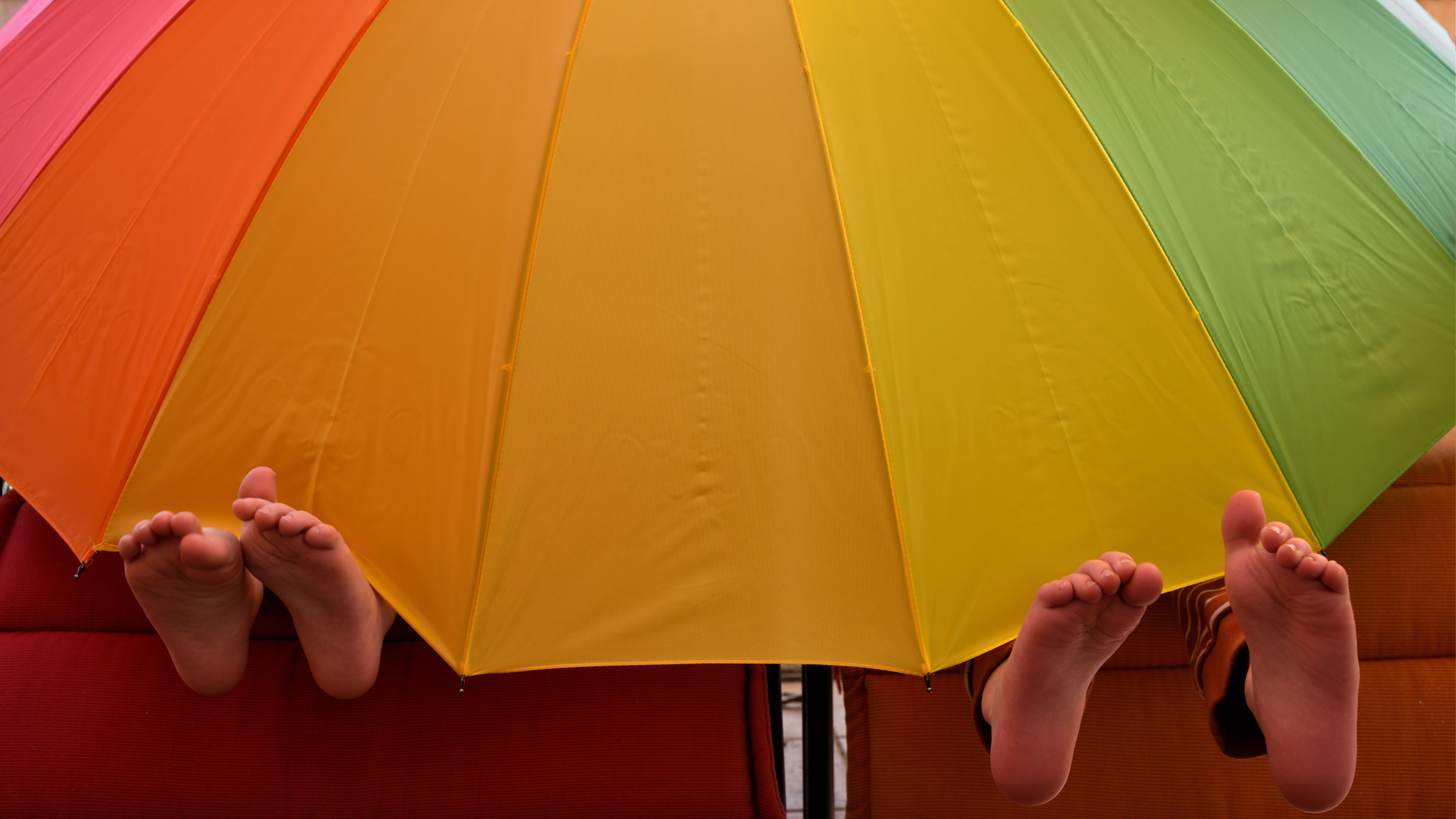Free Children's feet below a vibrant umbrella creating a playful scene outdoors. Stock Photo