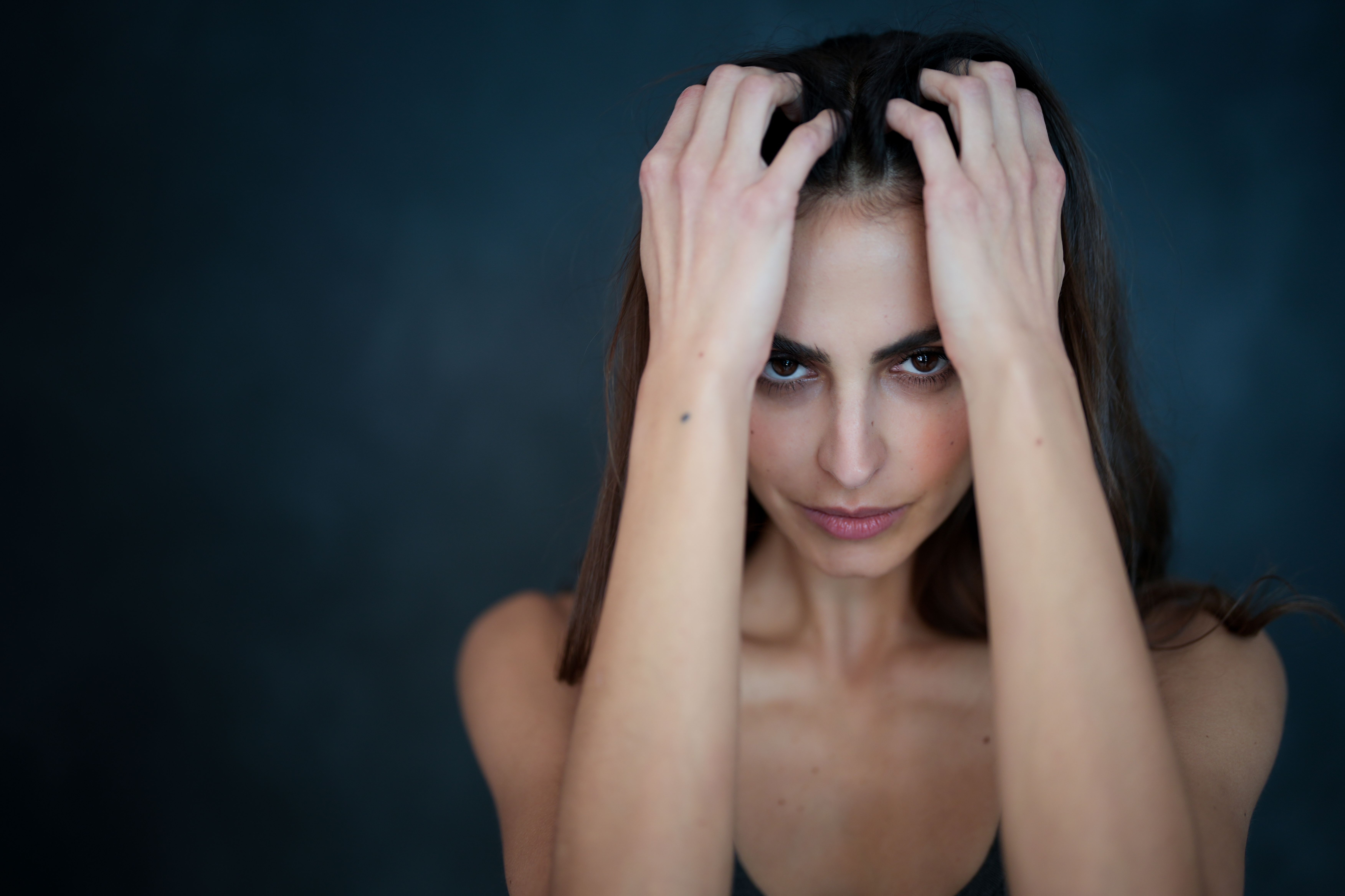 Striking portrait of a woman with long hair and hands in hair on a dark background.