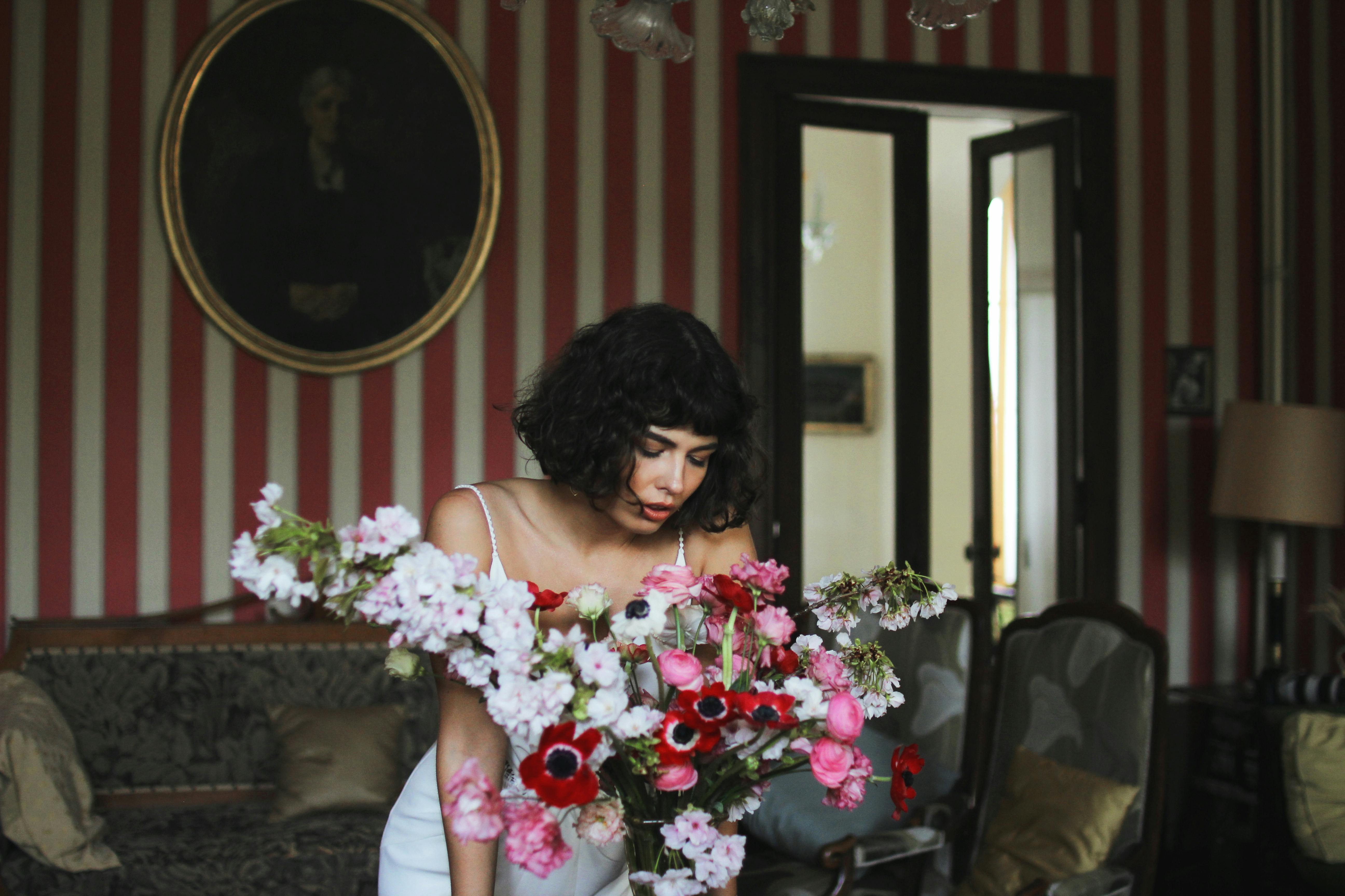 A woman arranges vibrant flowers in a vintage styled living room, adding a touch of elegance and color.
