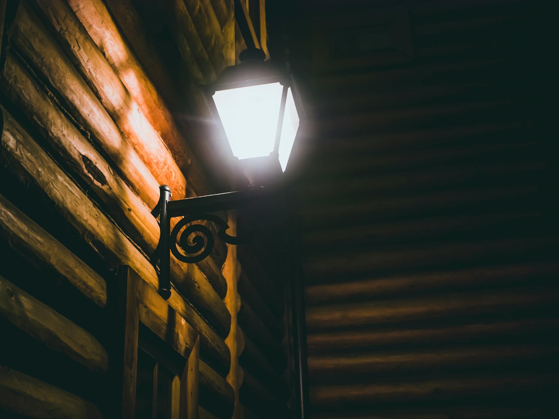 Charming vintage wall lamp on a wooden log cabin exterior at night, casting a warm glow.