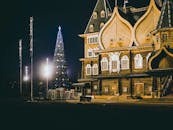 一棵装饰精美的圣诞树旁，矗立着一栋华丽的木制建筑，在夜间灯火通明