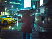 雨夜，一名撑伞的妇女走在城市街道上，映衬着城市生活