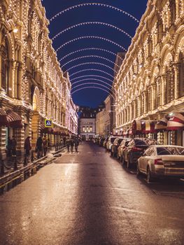 A beautifully lit street in Moscow with elegant buildings and string lights creating a warm ambiance at night.