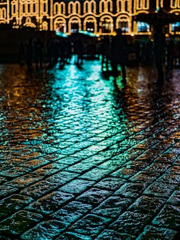 夜晚，鹅卵石街道被灯光照亮，倒影与剪影交织出戏剧性的氛围