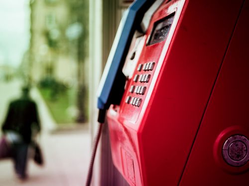 Free Vibrant red public telephone booth in urban setting with blurred background. Stock Photo