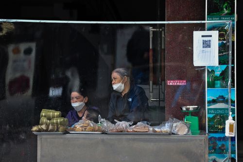 Free Masked street vendors in Vietnam sell traditional foods safely behind a protective screen. Stock Photo