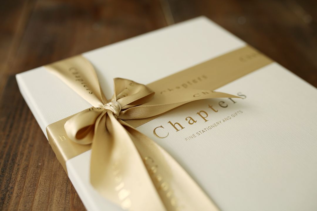 A close-up of an elegant gift box wrapped in a golden ribbon, placed on a wooden surface.