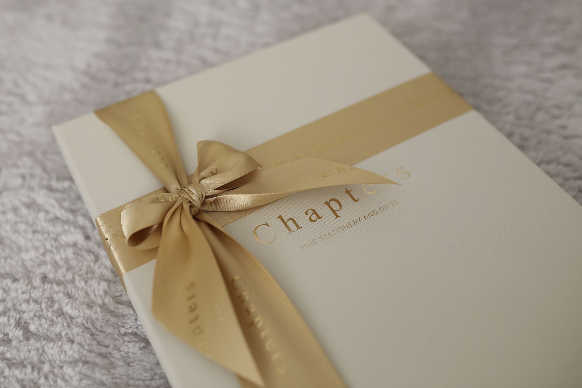 A beautifully wrapped gift box with gold ribbon and elegant stationery theme, perfect for special occasions.