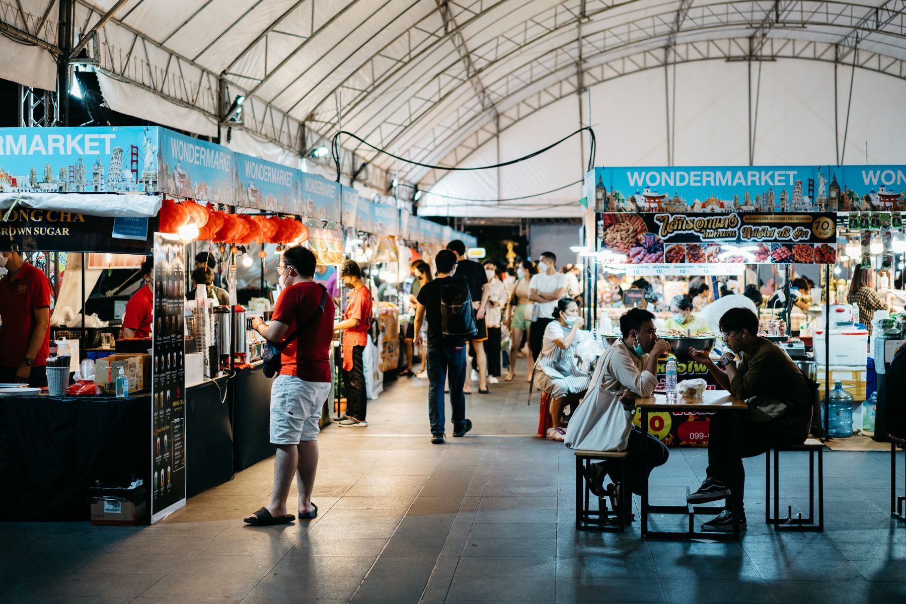 Diners eating beside multiple active food stalls in a lively Bangkok night market
