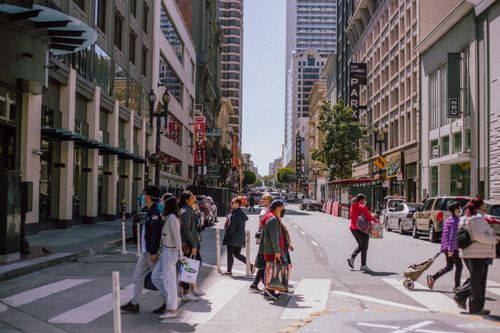 Free People crossing a city street at a bustling urban intersection during the day, showcasing modern architecture and city life. Stock Photo
