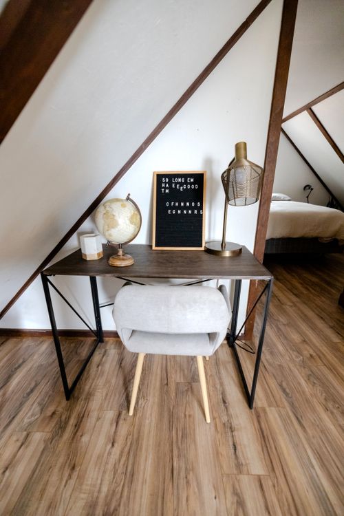 Free Stylish A-frame interior featuring a cozy desk setup with chair, lamp, globe, and board. Stock Photo