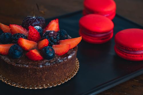 Free Close-up of a chocolate cake with fresh mixed berries and red macarons on the side. Stock Photo