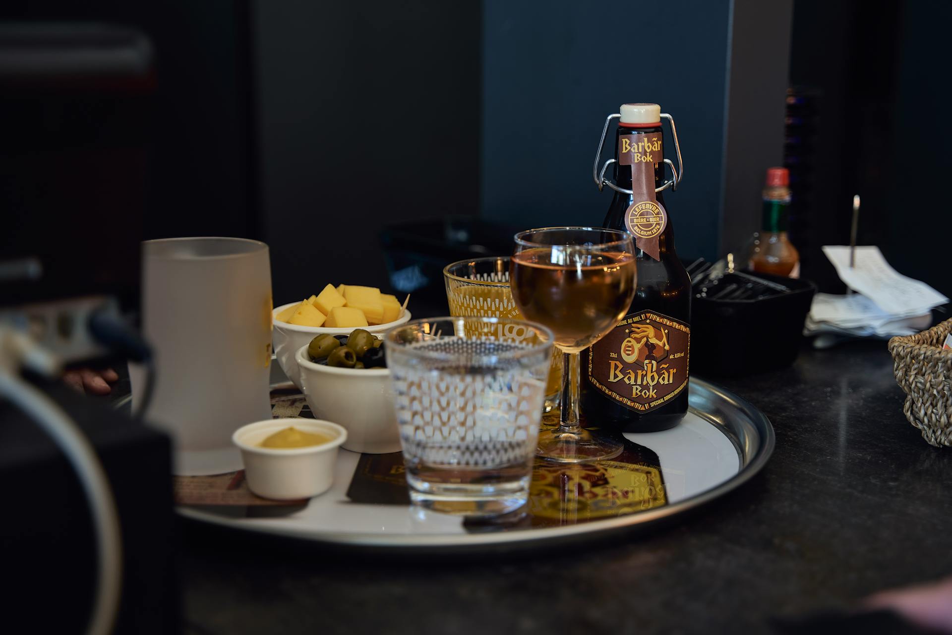 An elegant tray setup with a Barbar Bok bottle, glassware, olives, cheese, and snacks, perfect for a classy celebration.