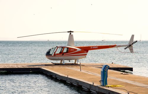 Free Red and white helicopter on a wooden dock overlooking a calm sea. Stock Photo