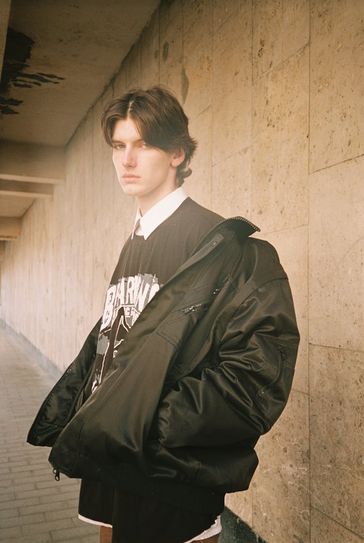 Young Man In Black Jacket Standing At Wall