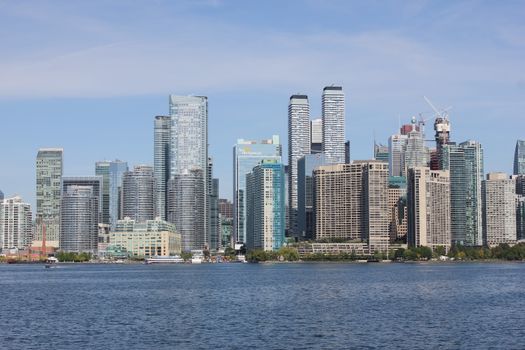 Toronto skyline with modern skyscrapers reflecting on Lake Ontario during the day.