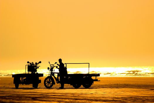 Silhouette of a person with tricycles on Mandarmani Beach during a glowing sunset.