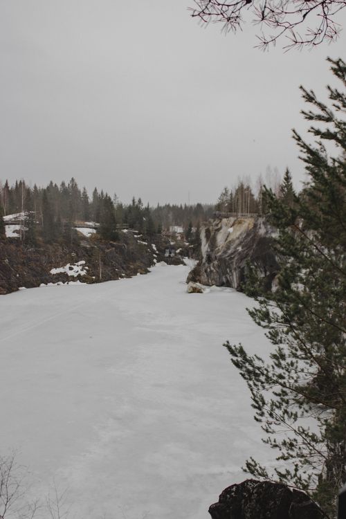 Free Snow-covered frozen river with rocky cliffs and pine trees during winter. Stock Photo
