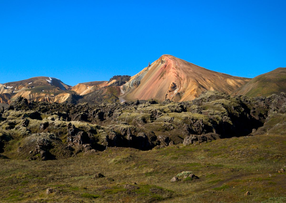 Brennisteinsalda's rhyolite slopes banded in orange, red, and green from ongoing hydrothermal alteration, rising over the dark lava field under a rare clear sky.