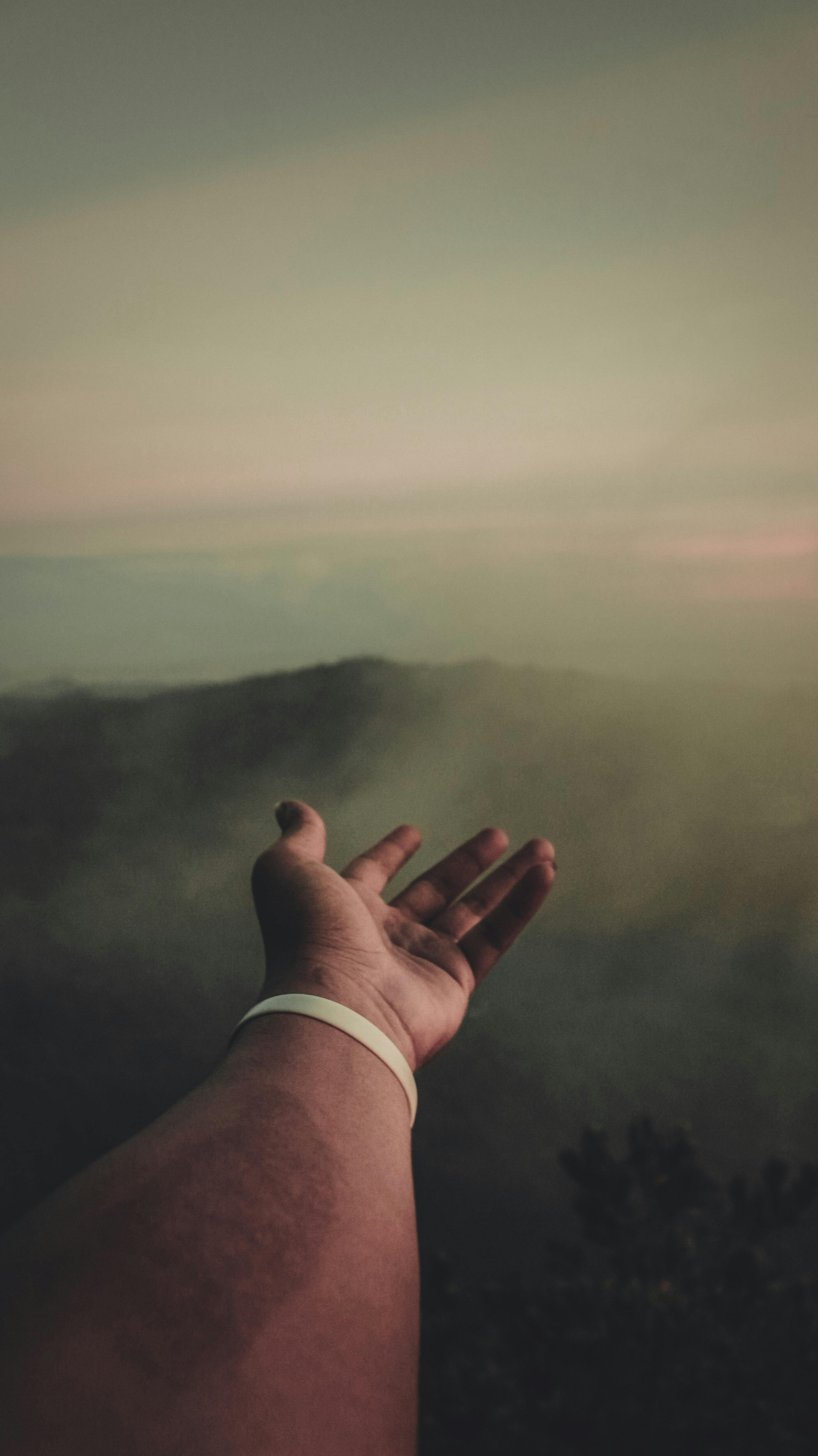 日落时分，一只手伸入雾霭笼罩的山间，营造出宁静而内省的景象
