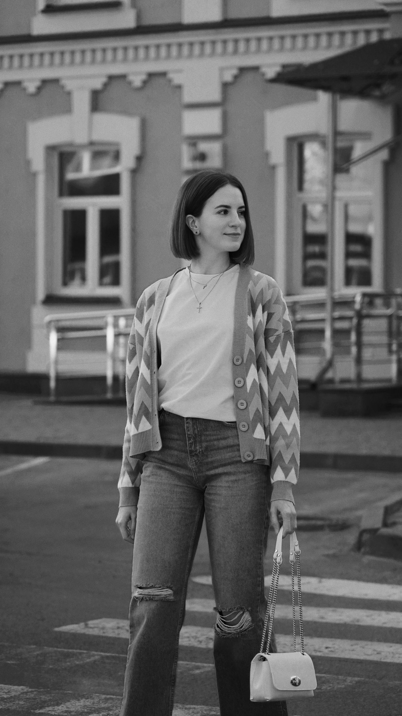 Woman in a chevron cardigan, white tee and ripped jeans with a chain bag