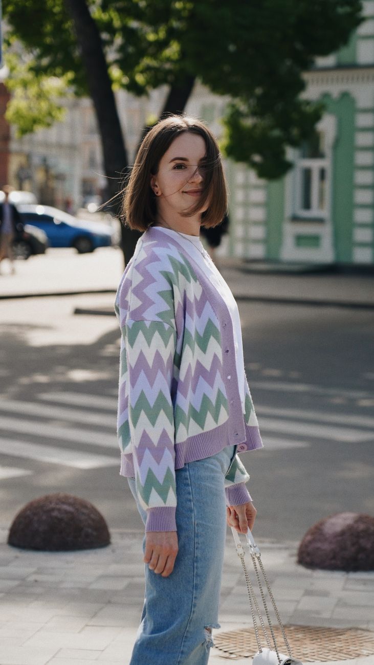 Smiling woman wearing a trendy zigzag cardigan, standing on a sunlit street.