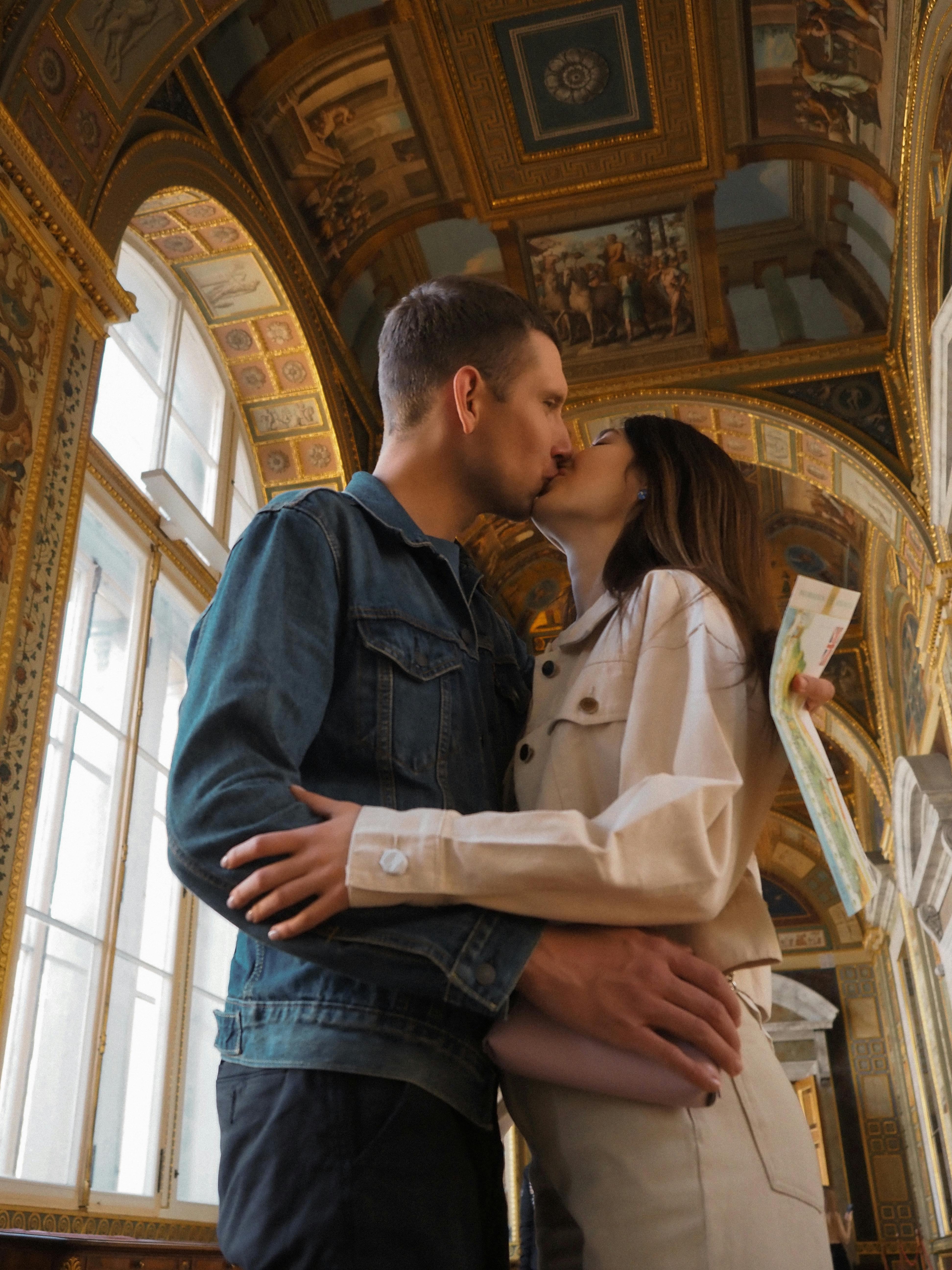 A couple embraces and kisses in an elegant museum corridor, adding a romantic touch to the artistic setting.