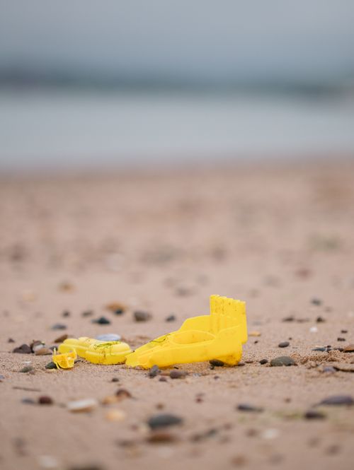 Free Yellow plastic toy excavator on a sandy beach with ocean in background. Stock Photo