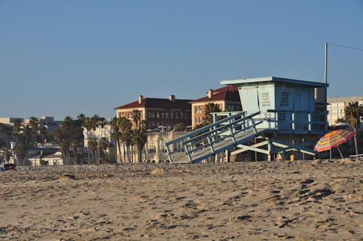 Lifeguard tower on Santa Monica beach with colorful umbrella and buildings in the background.
