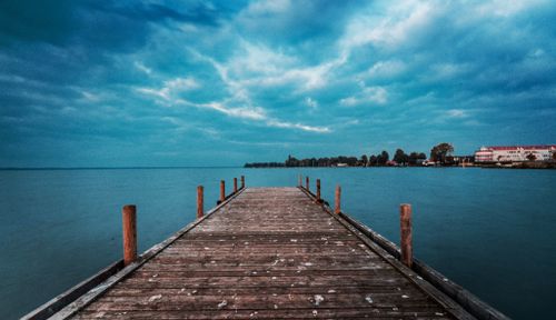Free A tranquil view of a wooden dock extending into a calm, vast ocean beneath a cloudy sky. Stock Photo