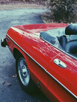 A shiny vintage red convertible car parked on a country road, showcasing classic design and style.