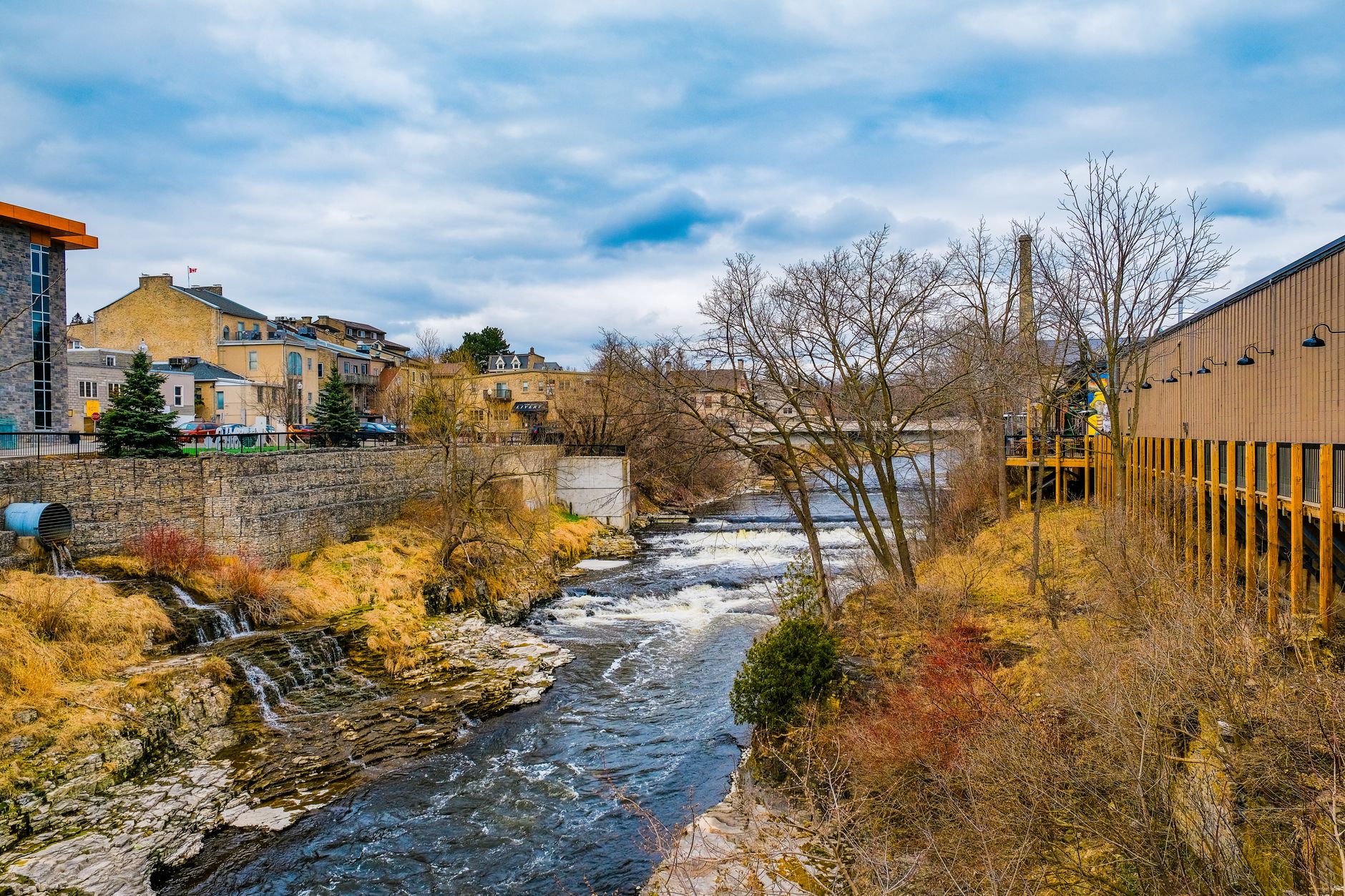 Scenic river view with historic architecture in Fergus, Ontario, highlighting nature and urban charm.