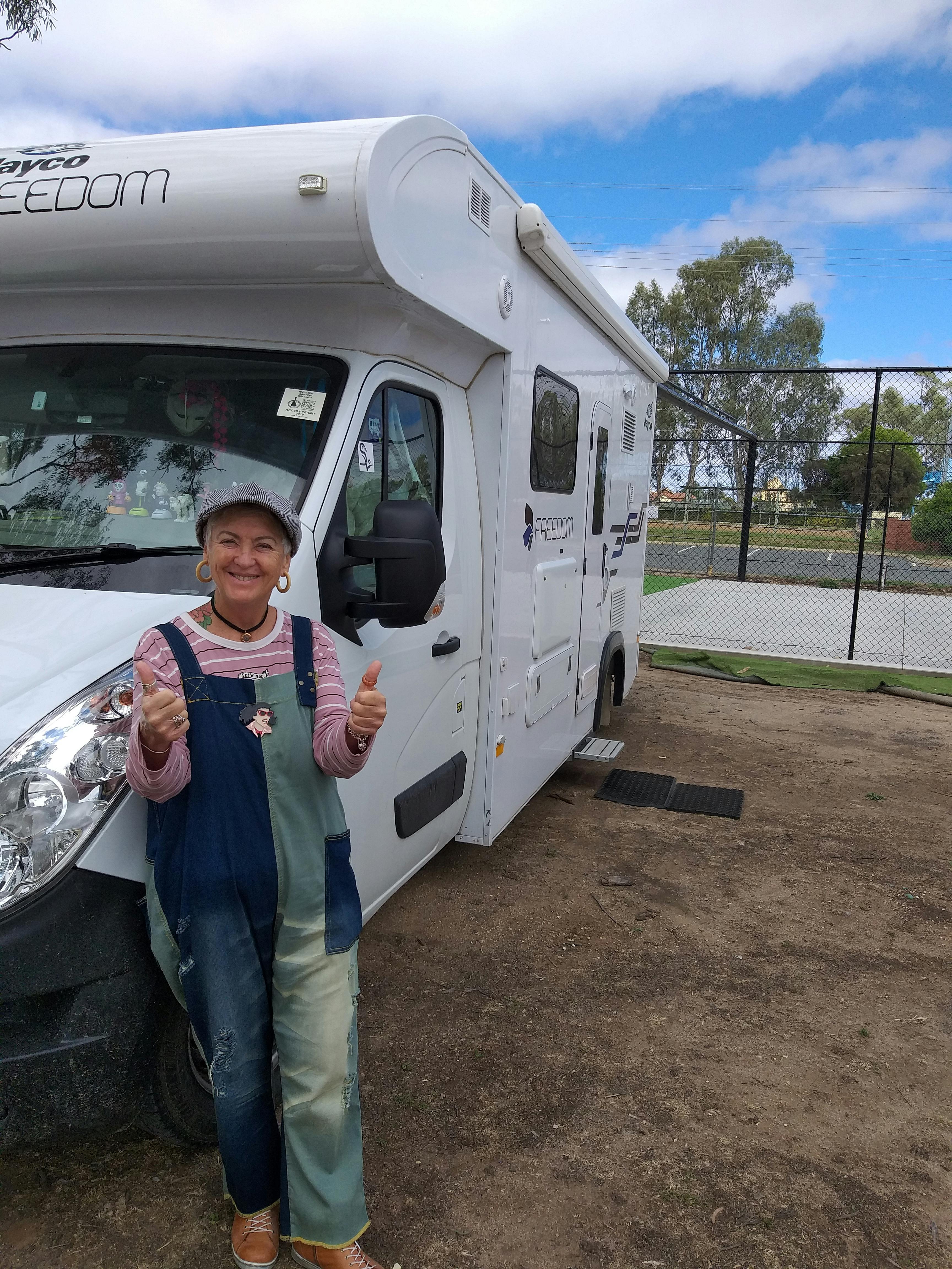 Senior woman giving thumbs up next to an RV in Cohuna, Australia, enjoying travel.