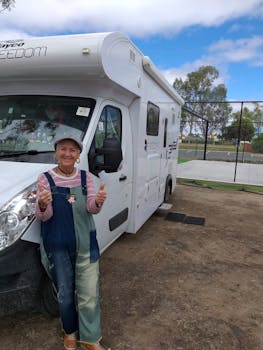 Senior woman giving thumbs up next to an RV in Cohuna, Australia, enjoying travel.