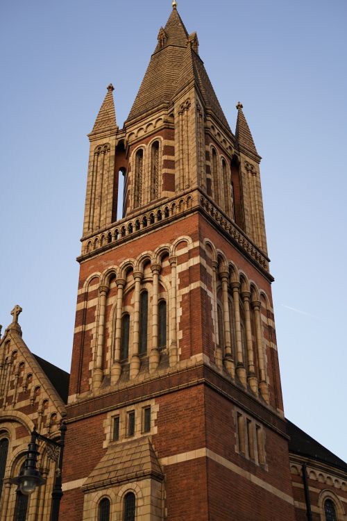 Free Vertical shot of a brick cathedral tower in Gothic Revival style against a clear blue sky. Stock Photo