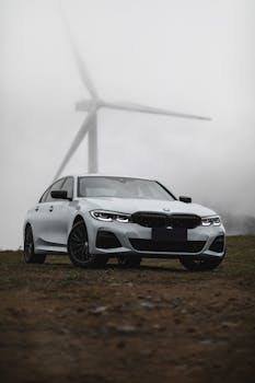 A modern BMW car parked in a foggy landscape with a wind turbine in the background, capturing a blend of technology and nature.