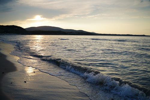 Free Tranquil sunset over a sandy beach with gentle waves lapping the shore. Stock Photo
