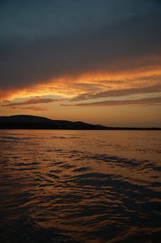 Captivating sunset with dramatic clouds over ocean and hills, perfect for serene wallpapers.