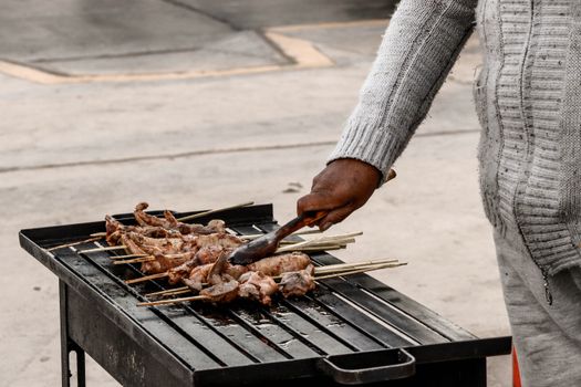 A street vendor grilling meat skewers on a charcoal barbecue outdoors.