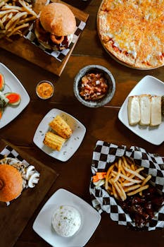 An inviting spread of American comfort food including burgers, fries, pizza, and corn.