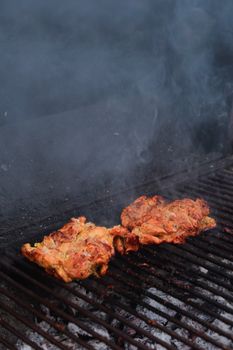 Close-up of seasoned chicken grilling outdoors, showcasing smoky texture.