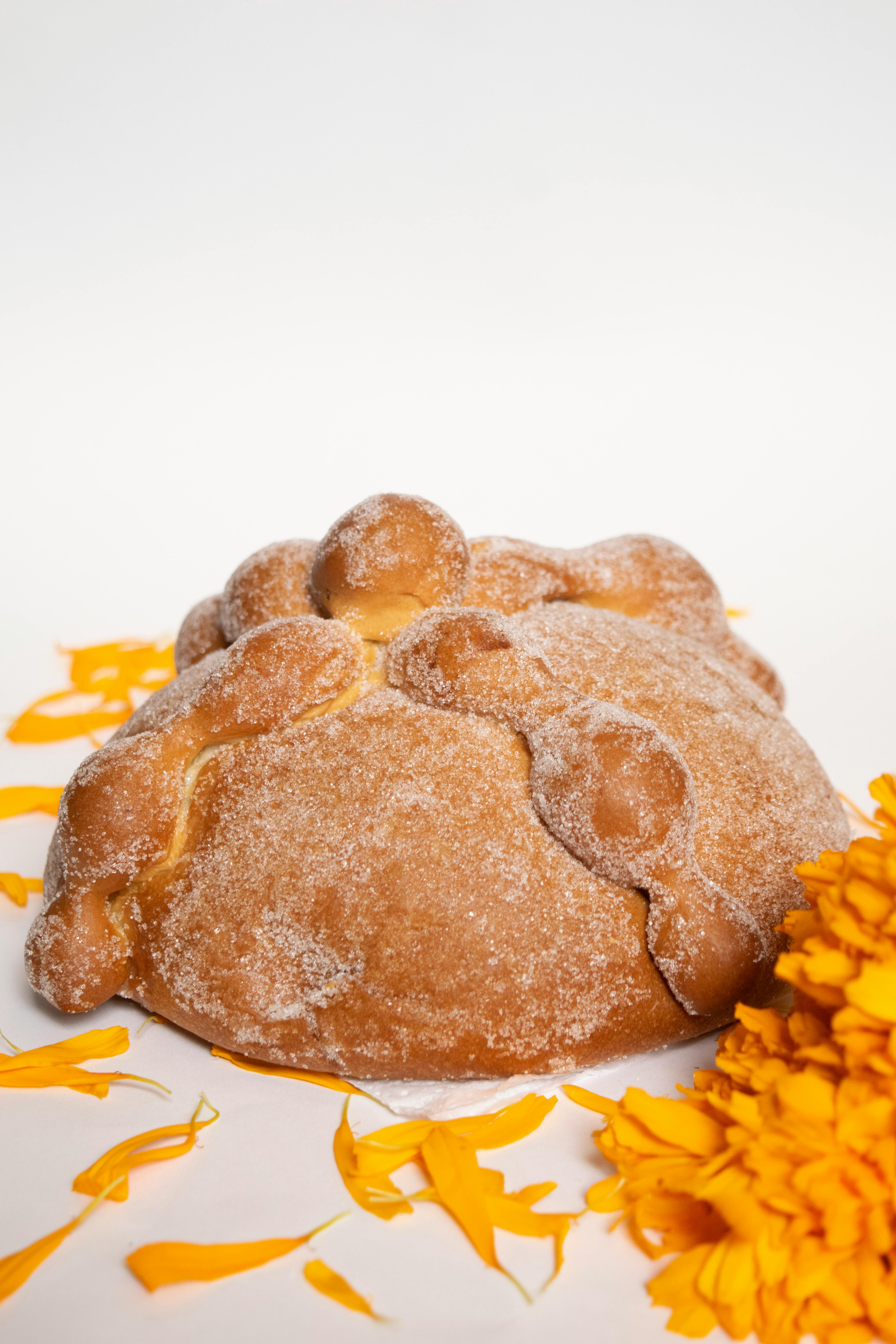 Pan de Muerto with marigold petals on a white background, capturing the essence of Día de los Muertos.