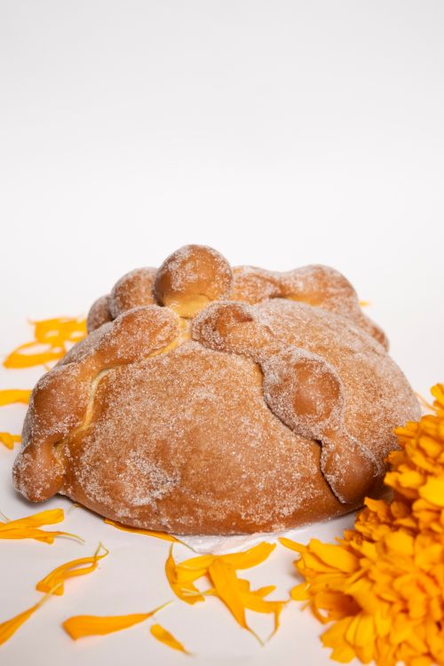 Free Pan de Muerto with marigold petals on a white background, capturing the essence of Día de los Muertos. Stock Photo