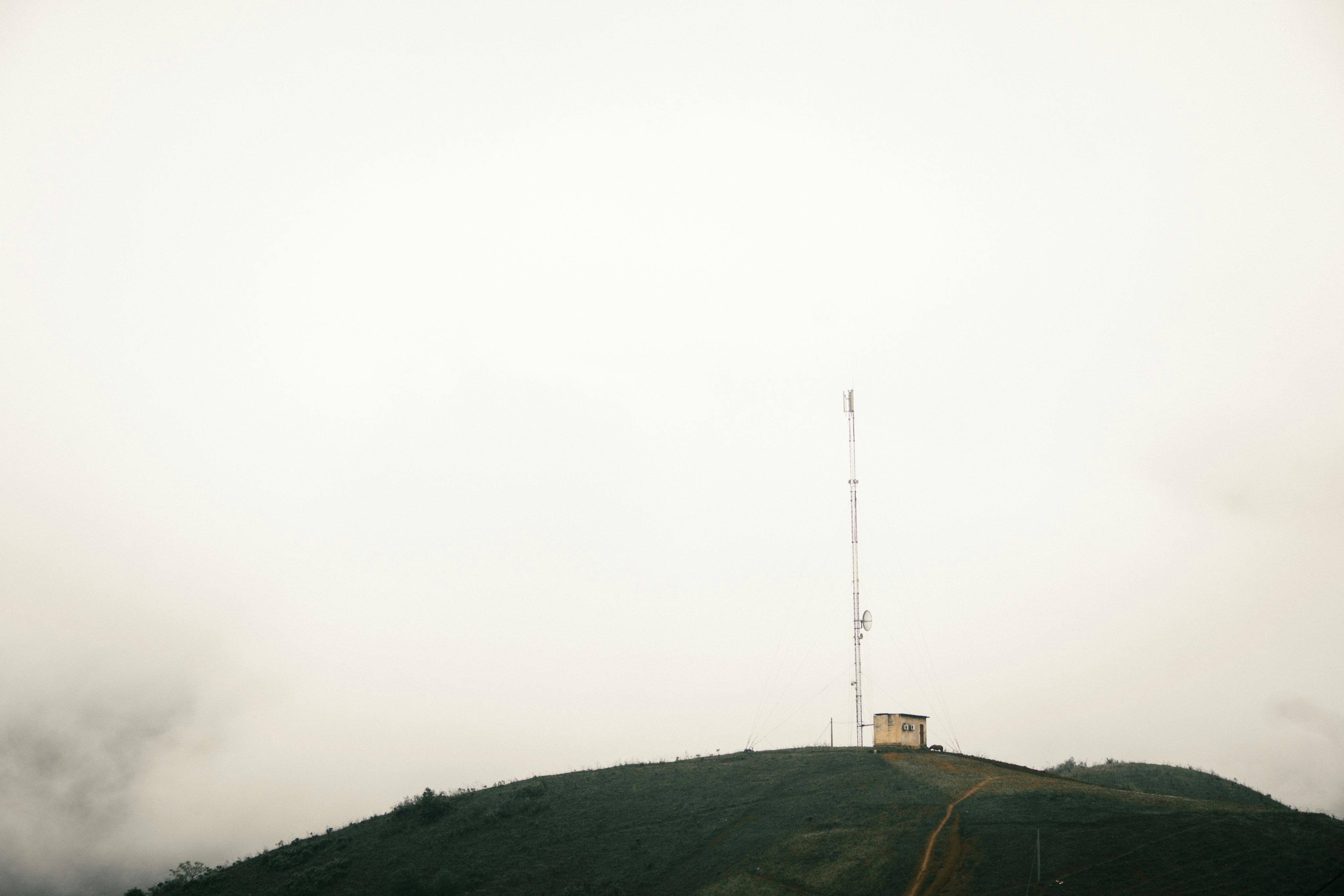 A misty hilltop featuring a telecommunication tower rising into the cloudy sky.