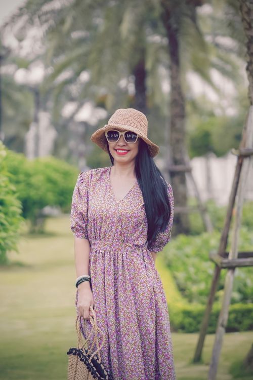Free Smiling woman wearing a floral dress and straw hat enjoying a sunny day outdoors. Stock Photo