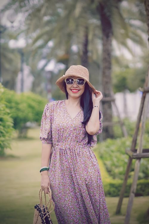 Free Woman in a floral dress and sun hat standing outdoors, embodying summer style. Stock Photo