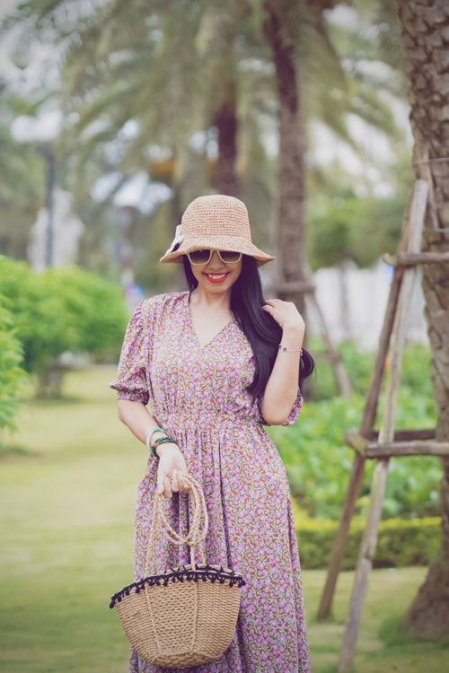 Free Fashionable woman with hat and wicker bag posing outdoors in a floral dress. Stock Photo