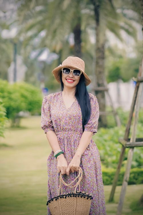 Free Stylish woman posing in a floral dress with woven accessories in a sunny park. Stock Photo