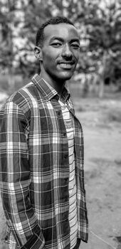 A smiling man in a plaid shirt, shot outdoors in black and white.